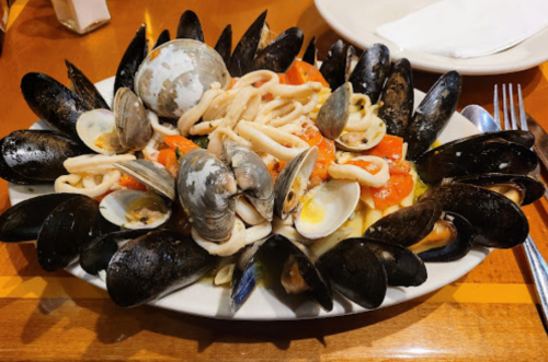 A seafood platter featuring mussels, clams, squid, and tomatoes arranged on a white plate.