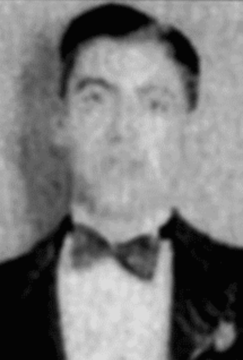 A blurred black-and-white portrait of a man in a tuxedo with a bow tie, looking directly at the camera.
