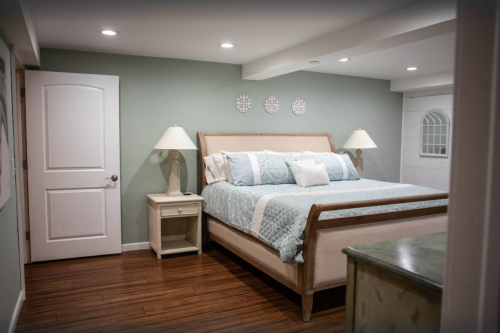Cozy bedroom with a large bed, light blue bedding, two lamps, and a green wall. Wood flooring adds warmth.