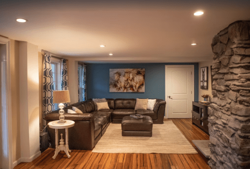 Cozy living room with a dark leather sectional, stone accent wall, and blue decor, featuring a light rug and artwork.