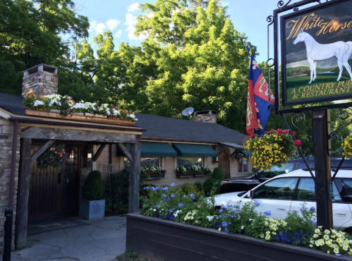 A charming country pub and restaurant with flower-filled planters and a sign featuring a white horse.