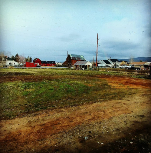 A rural landscape featuring a grassy field, a red barn, and scattered houses under a cloudy sky.