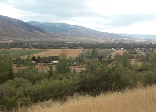 A scenic view of rolling hills and fields under a cloudy sky, with a small town visible in the valley below.