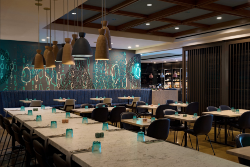 Modern restaurant interior featuring a long marble table, stylish lighting, and a vibrant mural on the wall.