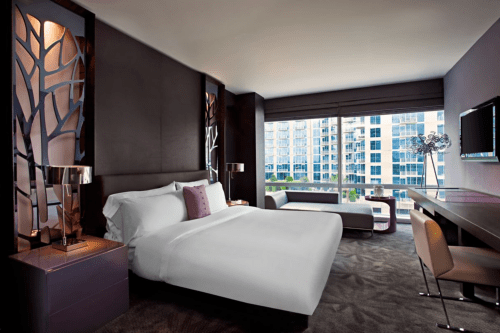 Modern hotel room featuring a king bed, stylish decor, large window with city view, and contemporary furnishings.