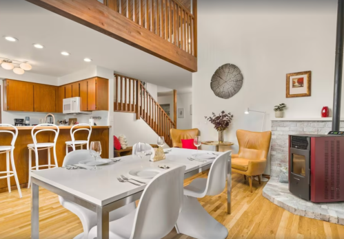 Modern dining area with a white table, stylish chairs, and a cozy living space featuring a fireplace and wooden accents.