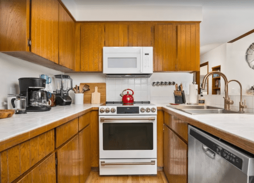 A cozy kitchen with wooden cabinets, a white stove, a red kettle, and various appliances on the counter.