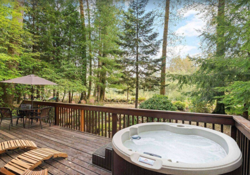 A wooden deck with a hot tub surrounded by lush green trees and a peaceful outdoor setting.