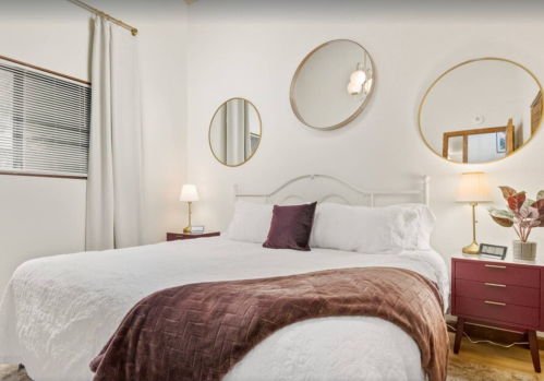 Cozy bedroom featuring a large bed, decorative mirrors, bedside lamps, and a plant in a vase.