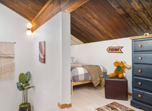 Cozy attic bedroom with wooden beams, a bed, a dresser, and decorative items including a plant and a stuffed moose.