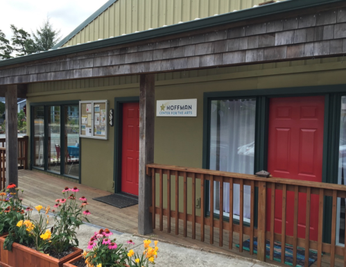 Exterior of the Hoffman Center for the Arts, featuring red doors, a wooden porch, and colorful flowers in front.