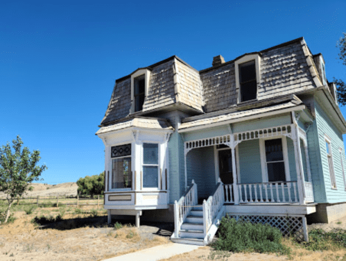 A vintage two-story house with a gabled roof, decorative trim, and a front porch, set against a clear blue sky.