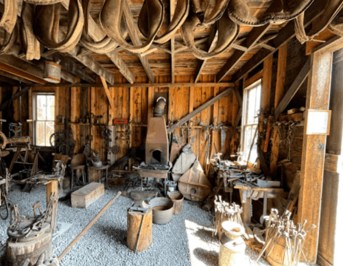 Interior of a rustic blacksmith shop with tools, an anvil, and wooden beams, creating a historical atmosphere.