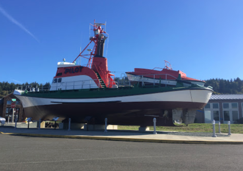 A large pilot boat displayed on land, painted red and green, with a clear blue sky in the background.