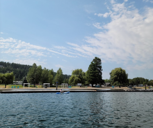 A serene lake view with a person kayaking, surrounded by trees and a clear blue sky.