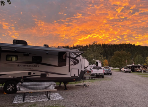 A campsite at sunset with an RV, picnic table, and vibrant orange and purple clouds in the sky.