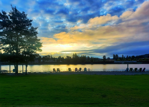 A serene lakeside view at sunset, with chairs lined up on the shore and colorful clouds reflecting on the water.
