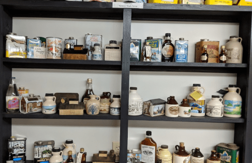 A display of vintage syrup containers and bottles on black shelves, showcasing various designs and sizes.