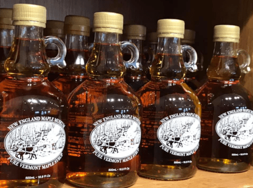 Bottles of pure Vermont maple syrup lined up on a shelf, each with a label featuring a winter scene.