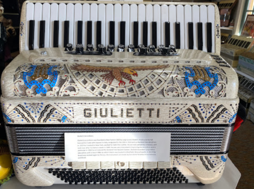 A beautifully decorated Giulietti accordion with intricate designs and a white finish, featuring black and white keys.