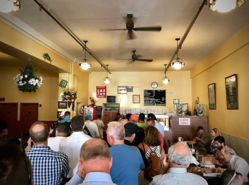 A crowded restaurant interior with people in line, vintage decor, and a menu board on the wall. Cash only sign visible.