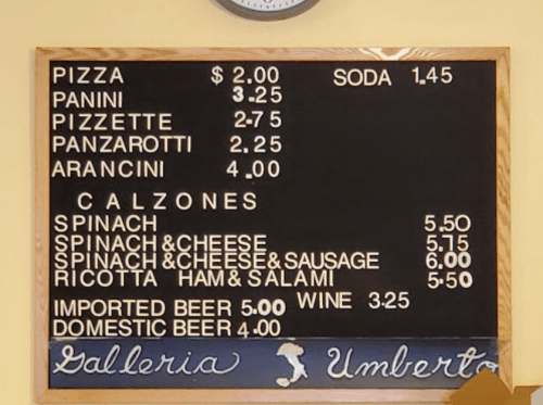 Menu board displaying prices for pizza, panini, calzones, and beverages at Galleria Umberto.