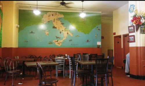 Interior of a restaurant featuring a colorful mural of Italy on the wall, with empty tables and chairs.