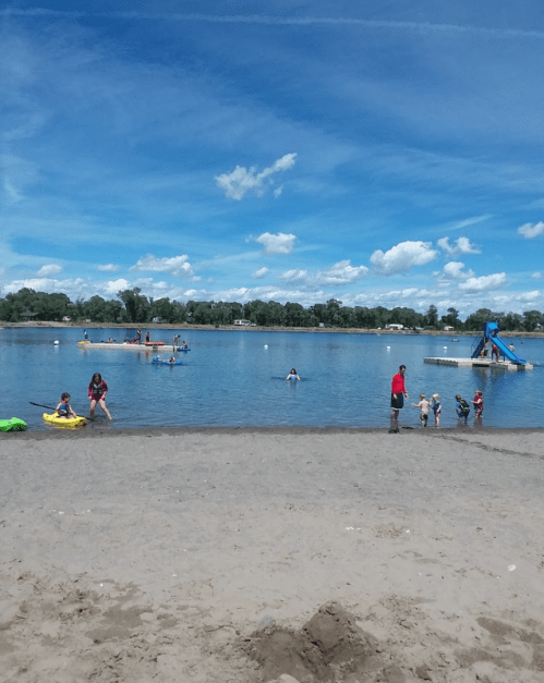 A sandy beach with children playing in the water and on the shore, under a blue sky with fluffy clouds.