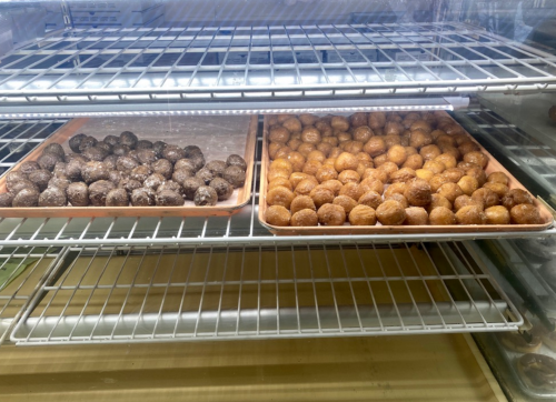 Two trays of round, coated snacks on a wire rack: one with dark chocolate and the other with a golden, sugary coating.