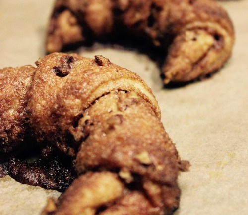 Close-up of a golden-brown, flaky croissant with a crispy texture on parchment paper.