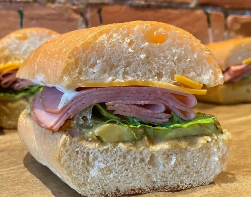 A close-up of a sandwich with layers of ham, cheese, lettuce, and pickles on a soft roll, cut in half.