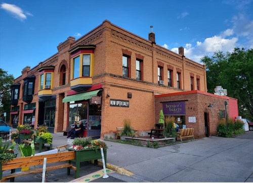 A colorful brick building with a bakery sign, surrounded by planters and a clear blue sky.