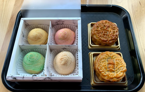 A tray with two types of pastries: colorful swirl buns and two golden mooncakes in decorative boxes.
