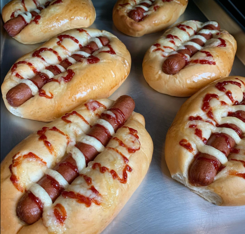 A tray of hot dogs in buns, topped with ketchup and mustard, freshly baked and golden brown.