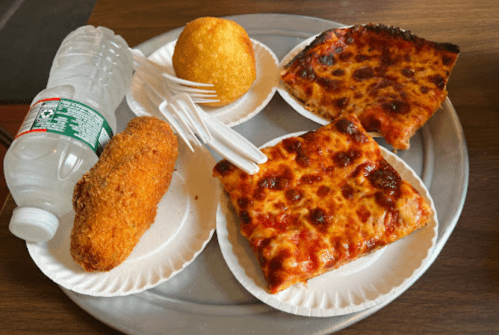 A metal tray with a slice of cheese pizza, a fried snack, a cornbread ball, and a water bottle.