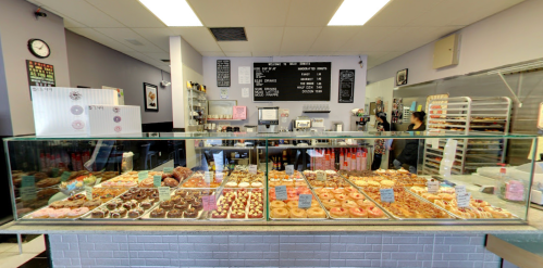 A bakery display case filled with various donuts and pastries, with a menu board and staff in the background.