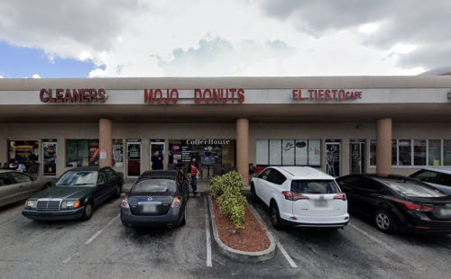 A storefront featuring "Mojo Donuts," "El Tiesto Cafe," and "Cleaners," with parked cars and people outside.