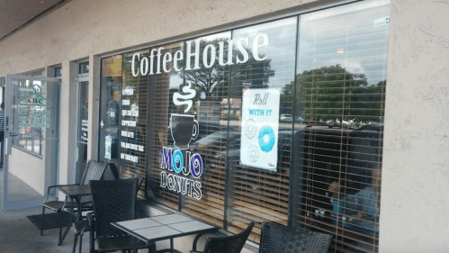 Exterior of a coffee house with a sign for "Mojo Donuts," featuring outdoor seating and large windows.