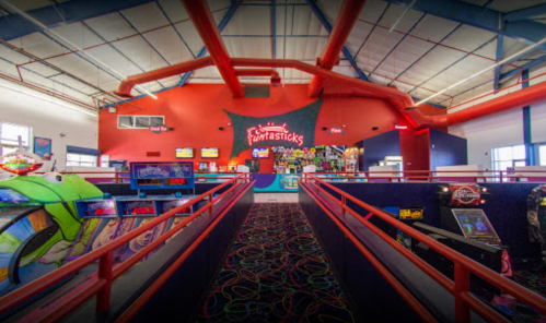Interior of an arcade with colorful decor, game machines, and a vibrant atmosphere. Red railings and a bright ceiling.