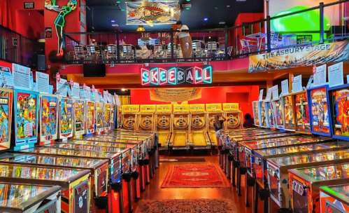 A vibrant arcade filled with pinball machines and skeeball lanes, featuring colorful lights and a lively atmosphere.