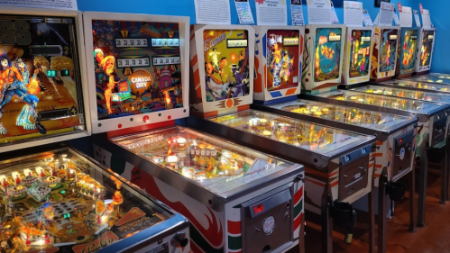 A row of vintage pinball machines with colorful designs and illuminated playfields in a retro arcade setting.