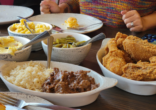 A table spread with fried chicken, rice, macaroni, green beans, and beef stew in various dishes.