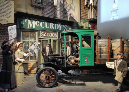 A vintage truck in a street scene with people holding protest signs outside a saloon, evoking a historical setting.