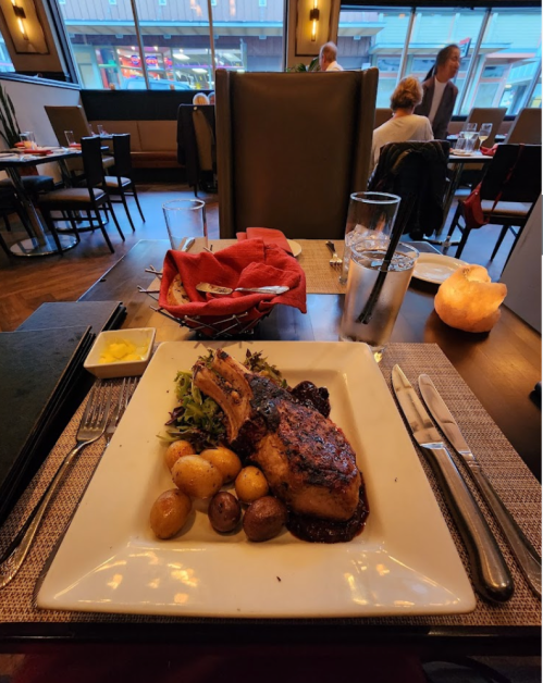 A plated meal featuring a grilled meat chop, roasted potatoes, and salad, set on a dining table in a restaurant.
