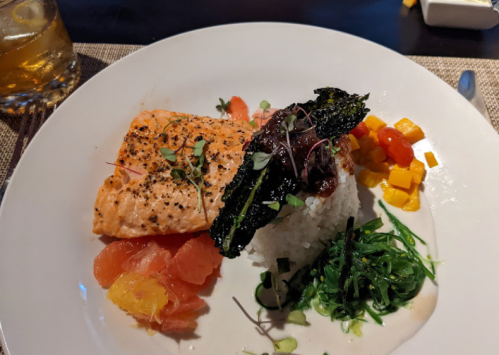 A plate featuring salmon, rice, seaweed, citrus segments, and diced mango, garnished with microgreens.