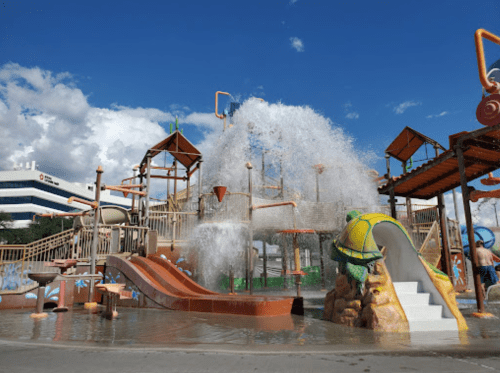 A vibrant water park with slides and a large splash feature under a blue sky.