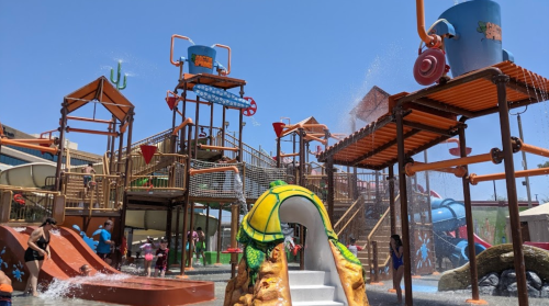 A vibrant water park with slides, splash features, and children playing under a clear blue sky.