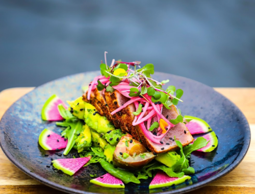 A beautifully plated dish featuring seared tuna, avocado, pickled onions, and vibrant watermelon radish slices.