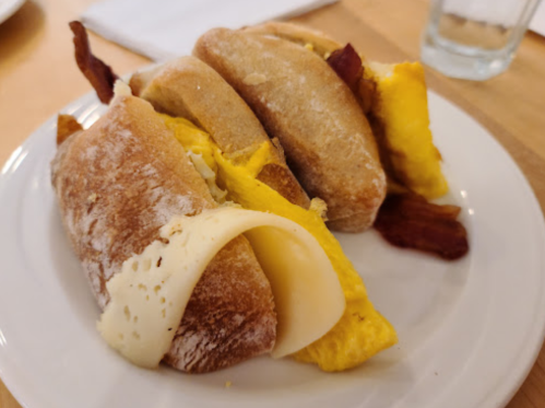 A plate with three sandwiches filled with eggs, cheese, and bacon on a toasted bun.