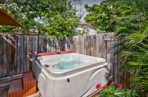 A hot tub surrounded by a wooden fence and lush greenery, with potted plants nearby.